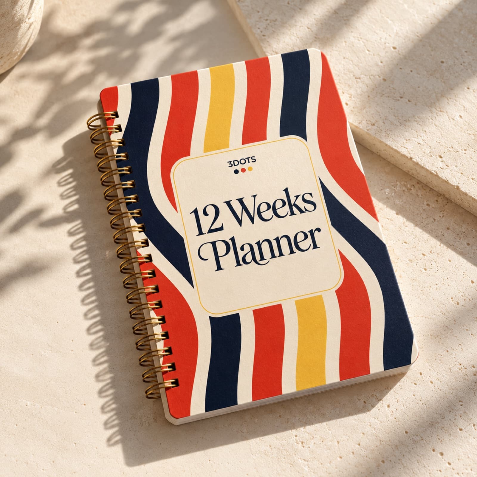 12 Weeks Planner with a navy, red, and yellow striped cover and gold spiral binding